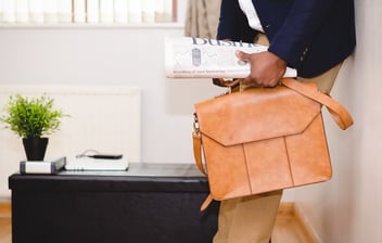 investor leaning on wall with briefcase and newspaper