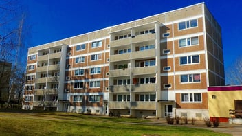 brown apartment complex building with green lawn under blue sky